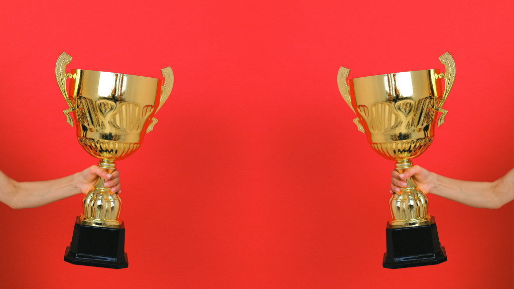 Two hands hold rewards trophies on a red background